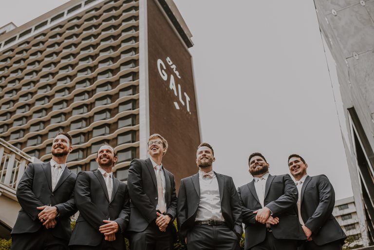 Groomsmen look off into the distance with the Galt House Hotel behind them
